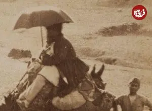 عکس| سفر زمان؛ زن و مرد کجاوه‌سوار و مردی با چتر در حال سفر با کاروان؛ بیش از 100 سال قبل