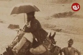 عکس| سفر زمان؛ زن و مرد کجاوه‌سوار و مردی با چتر در حال سفر با کاروان؛ بیش از 100 سال قبل